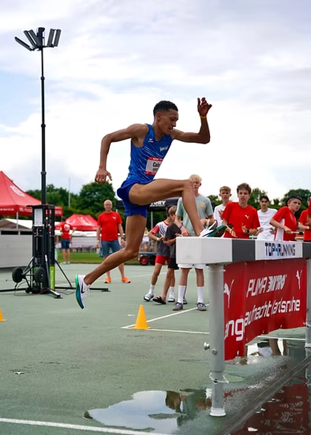 Der Laufcoach - Leistungscoaching und Analyse für Läufer - Ein Athlet in einem blauen Singlet springt während eines Hindernislaufs in der Leichtathletik über eine Hürde.