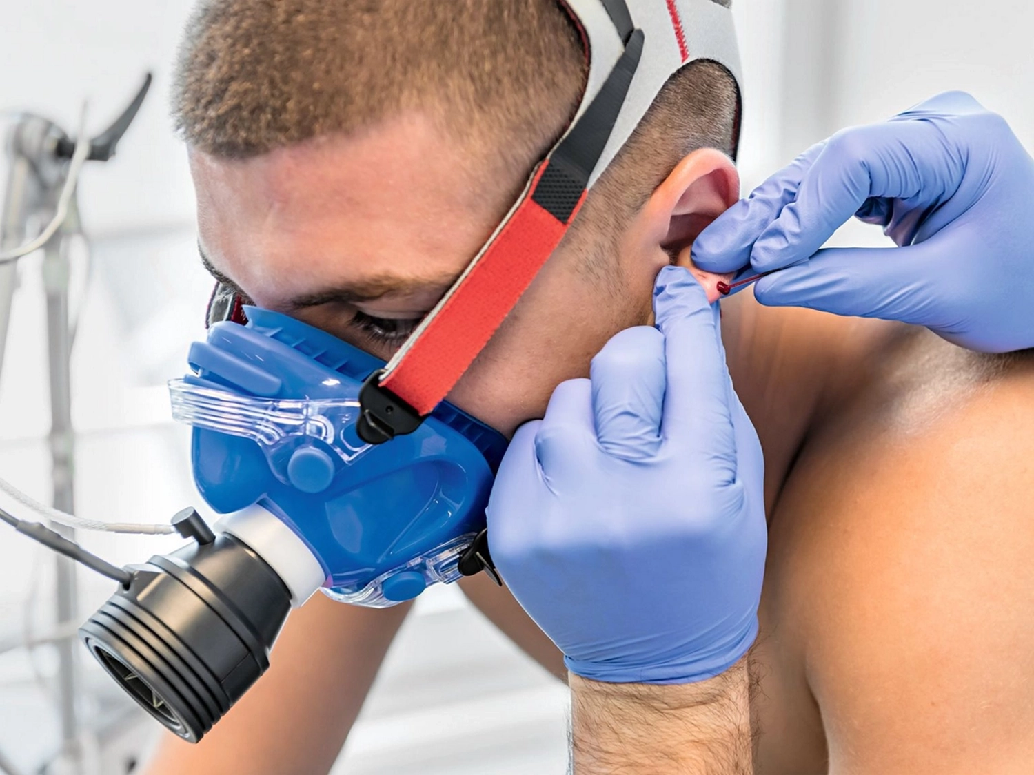 Der Laufcoach - Leistungscoaching und Analyse für Läufer - Ein Sportler trägt eine Sauerstoffmaske, während ein Arzt mit blauen Handschuhen ihm eine Blutprobe aus dem Ohrläppchen entnimmt.