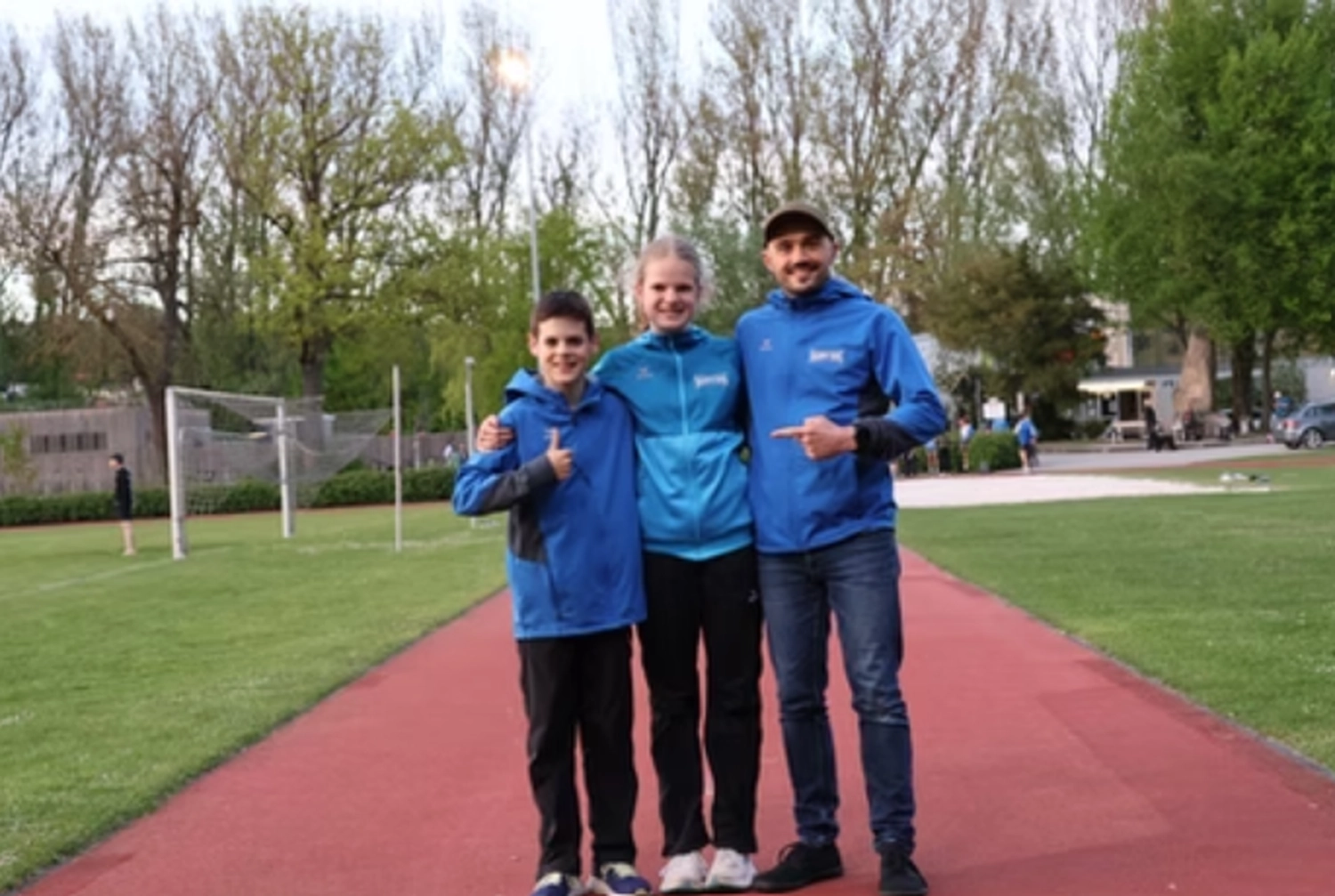 Der Laufcoach - Leistungscoaching und Analyse für Läufer - Ein Mann und zwei Kinder posieren für ein Foto auf einer roten Laufbahn auf einem Sportplatz im Freien.
