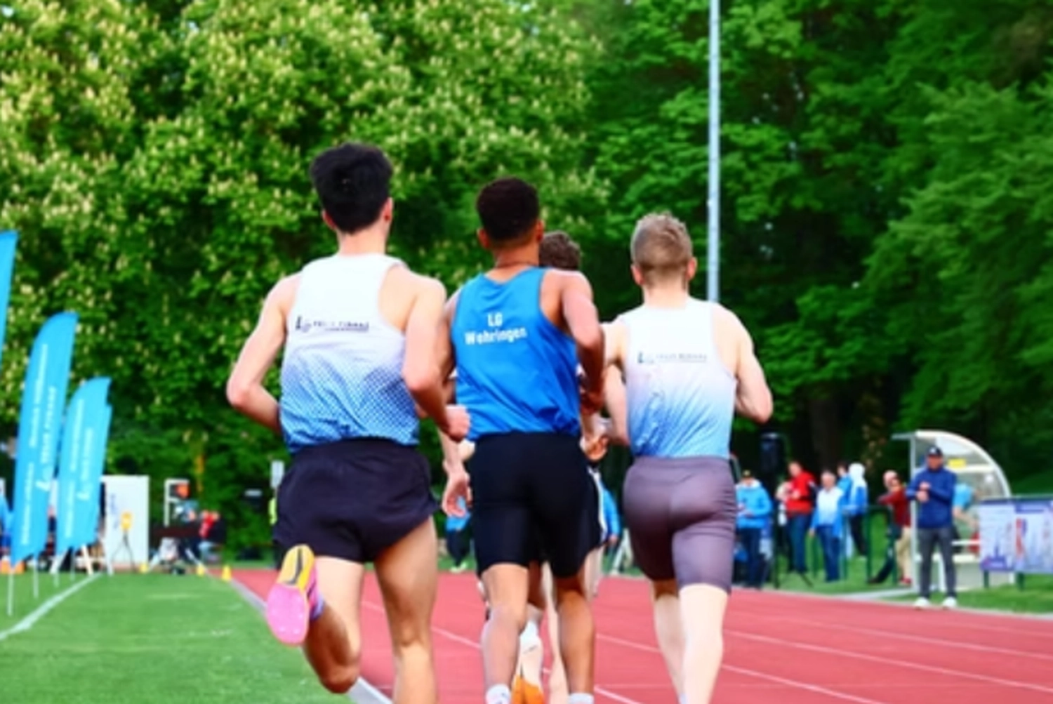 Der Laufcoach - Leistungscoaching und Analyse für Läufer - Eine Gruppe von Läufern in Sportkleidung rast eine Freiluftbahn entlang, von hinten gefilmt.