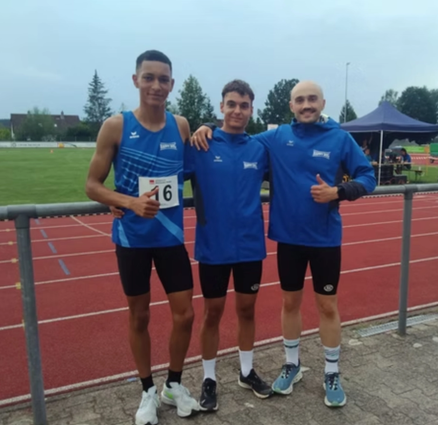 Der Laufcoach - Leistungscoaching und Analyse für Läufer - Drei sportliche junge Männer posieren gemeinsam auf einer Freiluftlaufbahn, alle tragen die gleichen blauen Sportoberteile und schwarze Sportshorts.