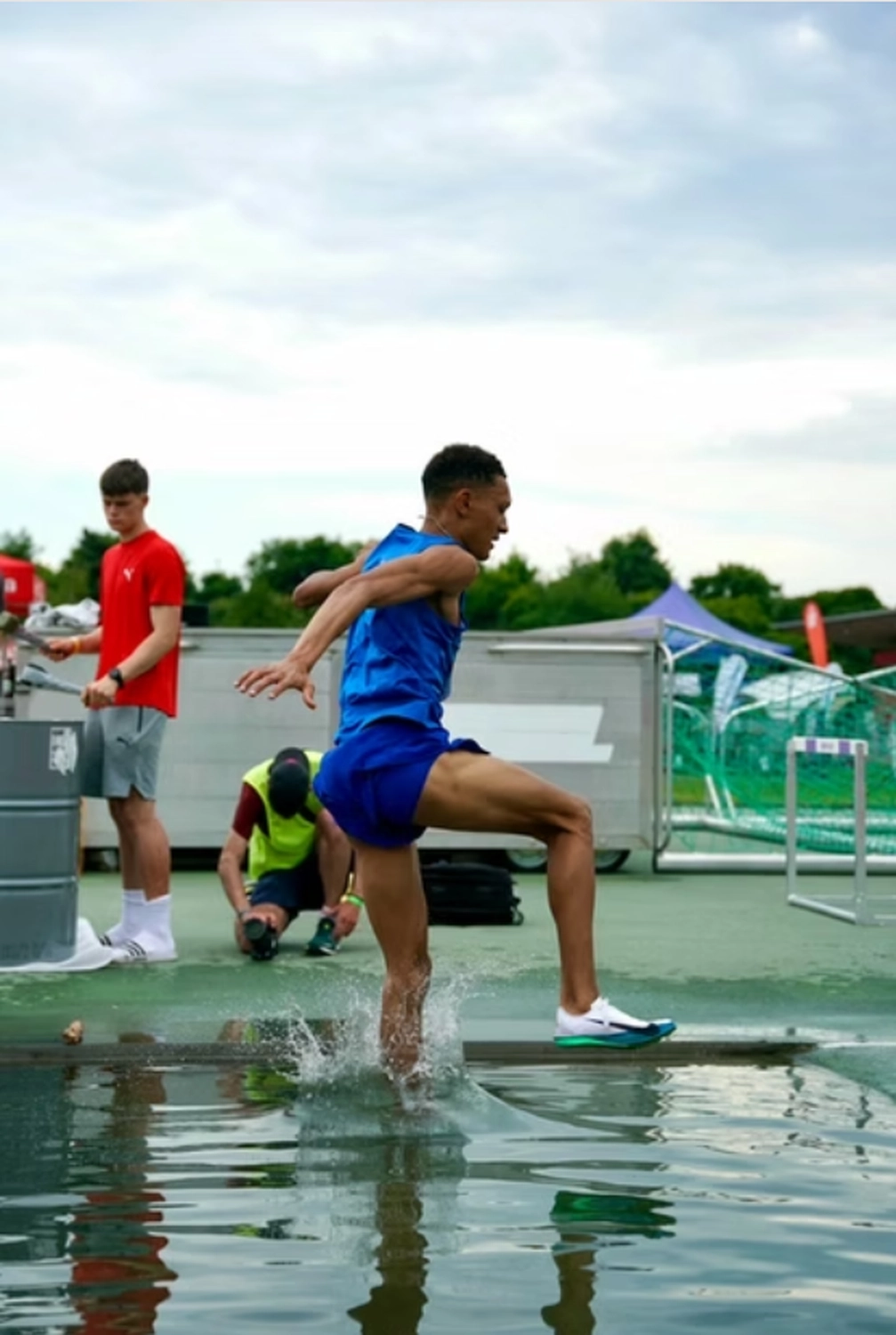 Der Laufcoach - Leistungscoaching und Analyse für Läufer - Ein Athlet in blauer Sportkleidung springt während eines Hindernislaufs auf einer Freiluftbahn über eine Hürde in einen Wassergraben.